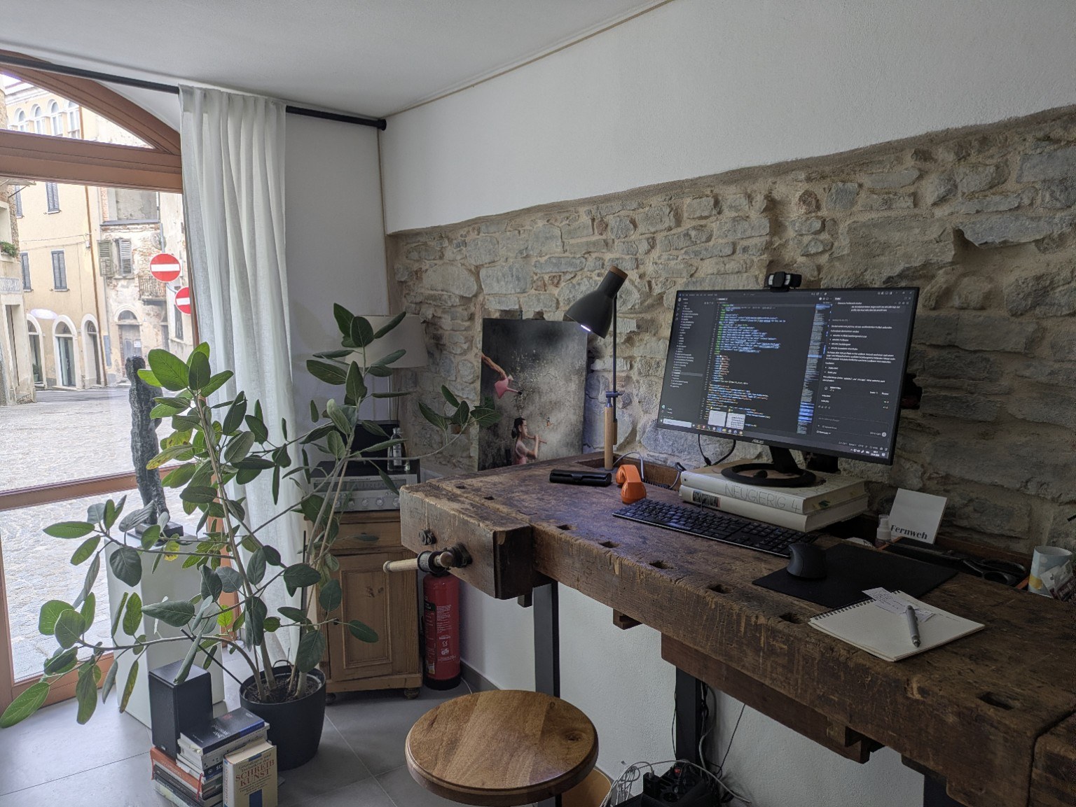 Postazione di lavoro di ServoDigitale a Murazzano con banco da lavoro, computer, parete in pietra e vista sulla strada.